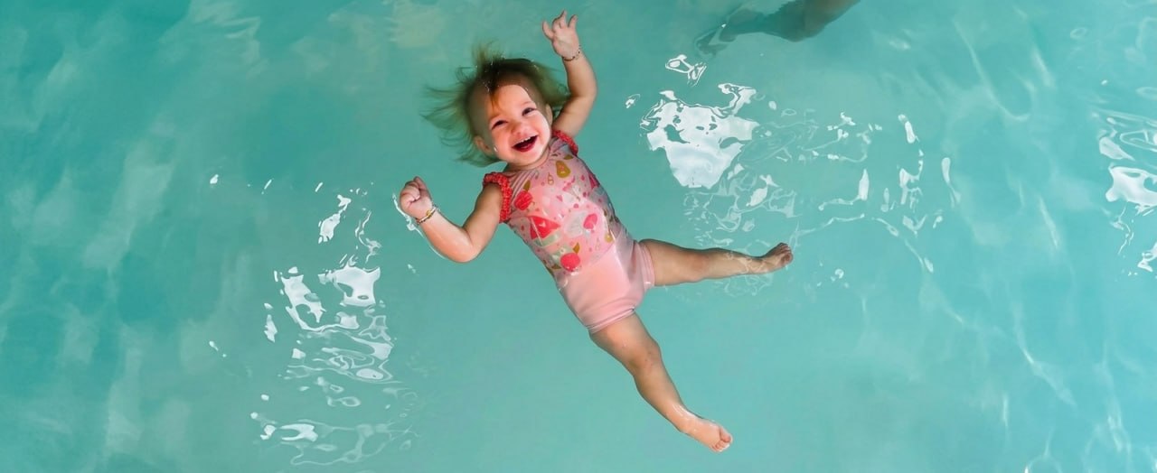 A happy toddler floating on her back in the pool with a big smile during an ISR lesson