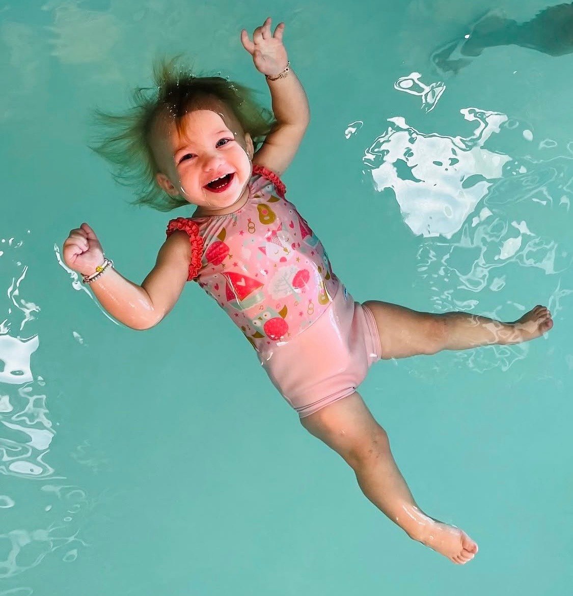 A happy baby girl floating on her back in a pink swimsuit during ISR lesson